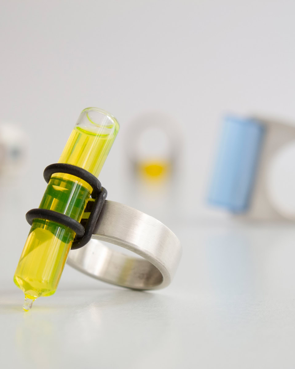 Création de bague en argent avec un tube à essai jaune, floue en arrière-plan d'autres bagues similaires.