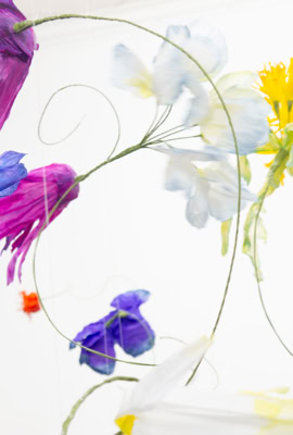 Fleurs colorées en papier suspendues dans les airs sur un fond blanc.