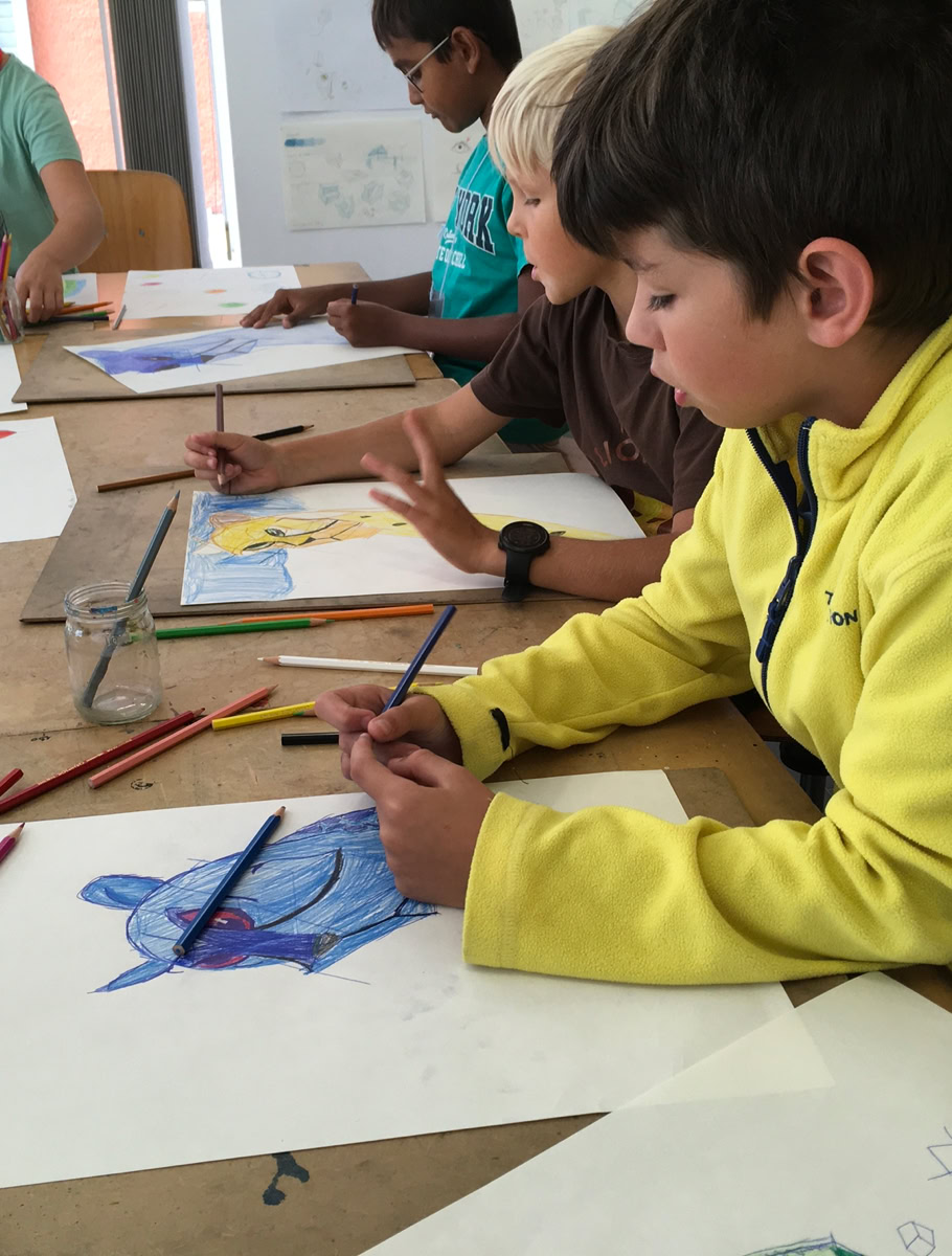 Des enfants assis à une table en train de dessiner avec des crayons de couleur.