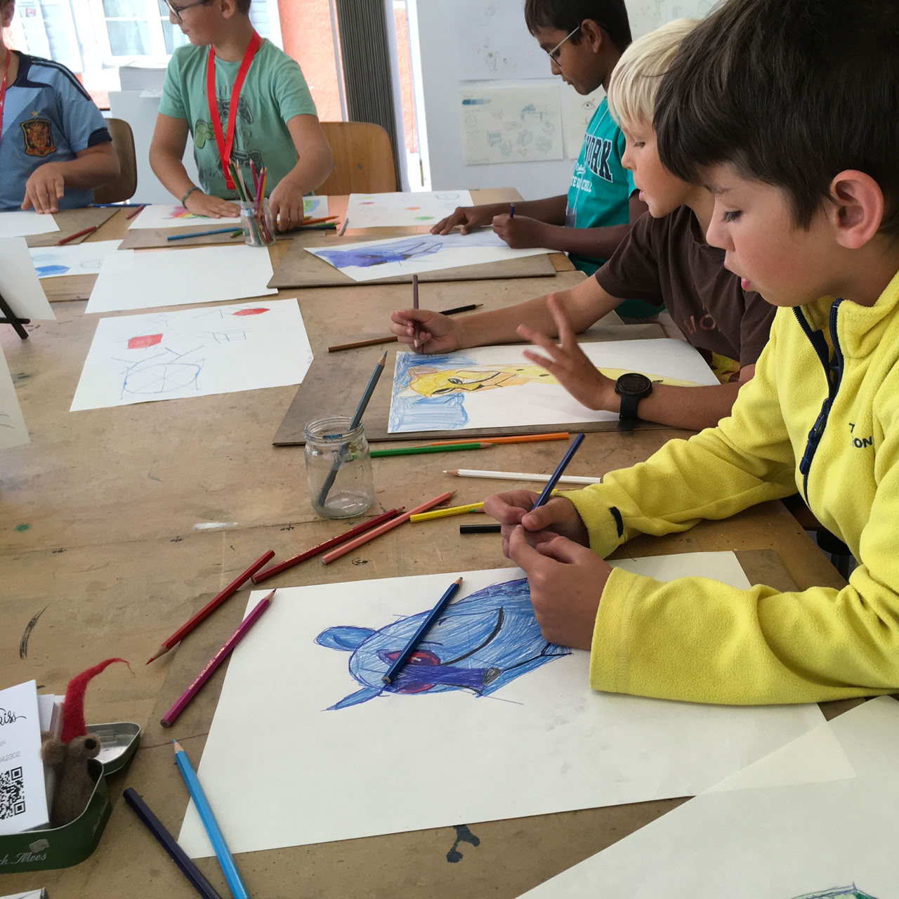 Des enfants assis à une table en train de dessiner avec des crayons de couleur.