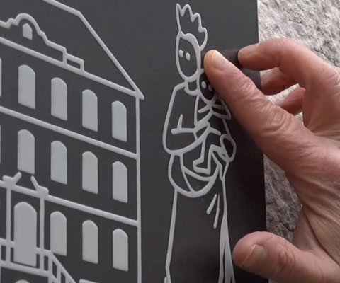 Main tenant une plaque avec des dessins en relief d'un bâtiment et d'une figure humaine.