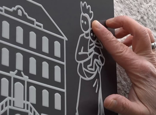 Main tenant une plaque avec des dessins en relief d'un bâtiment et d'une figure humaine.