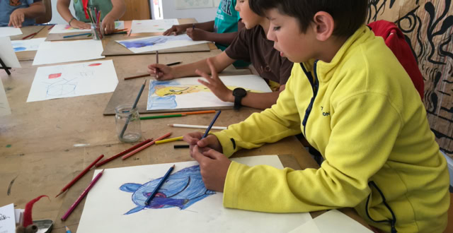 Des enfants assis à une table en train de dessiner avec des crayons de couleur.