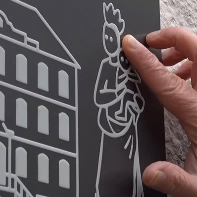 Main tenant une plaque avec des dessins en relief d'un bâtiment et d'une figure humaine.