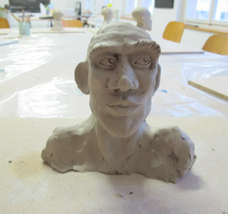 Buste en argile d'une tête humaine sur une table, avec des chaises en arrière-plan.