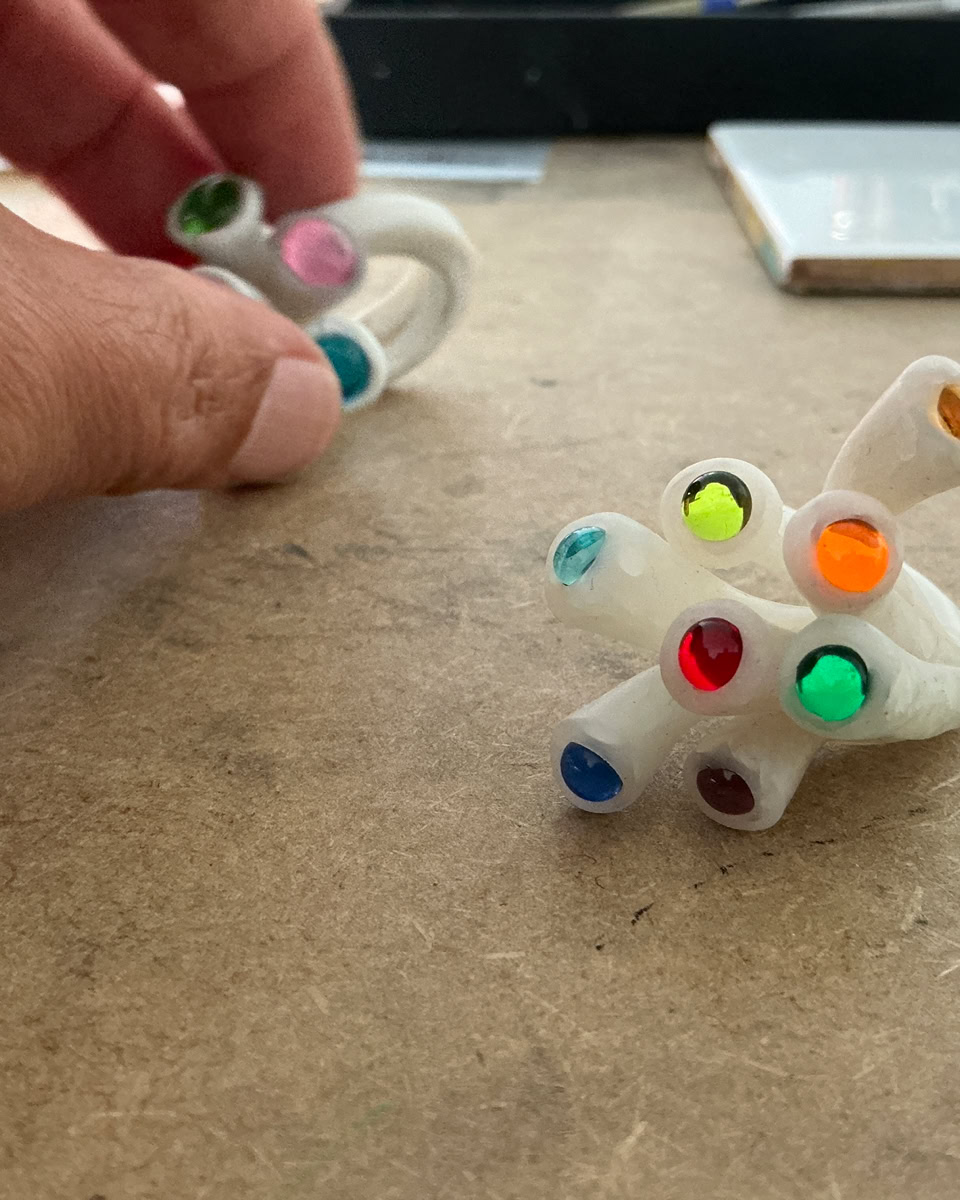 Main tenant une bague en résine blanc avec des perles colorés, posé sur une surface en bois.