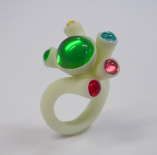 Bague blanche avec des pierres colorées vertes, rouges et bleues.