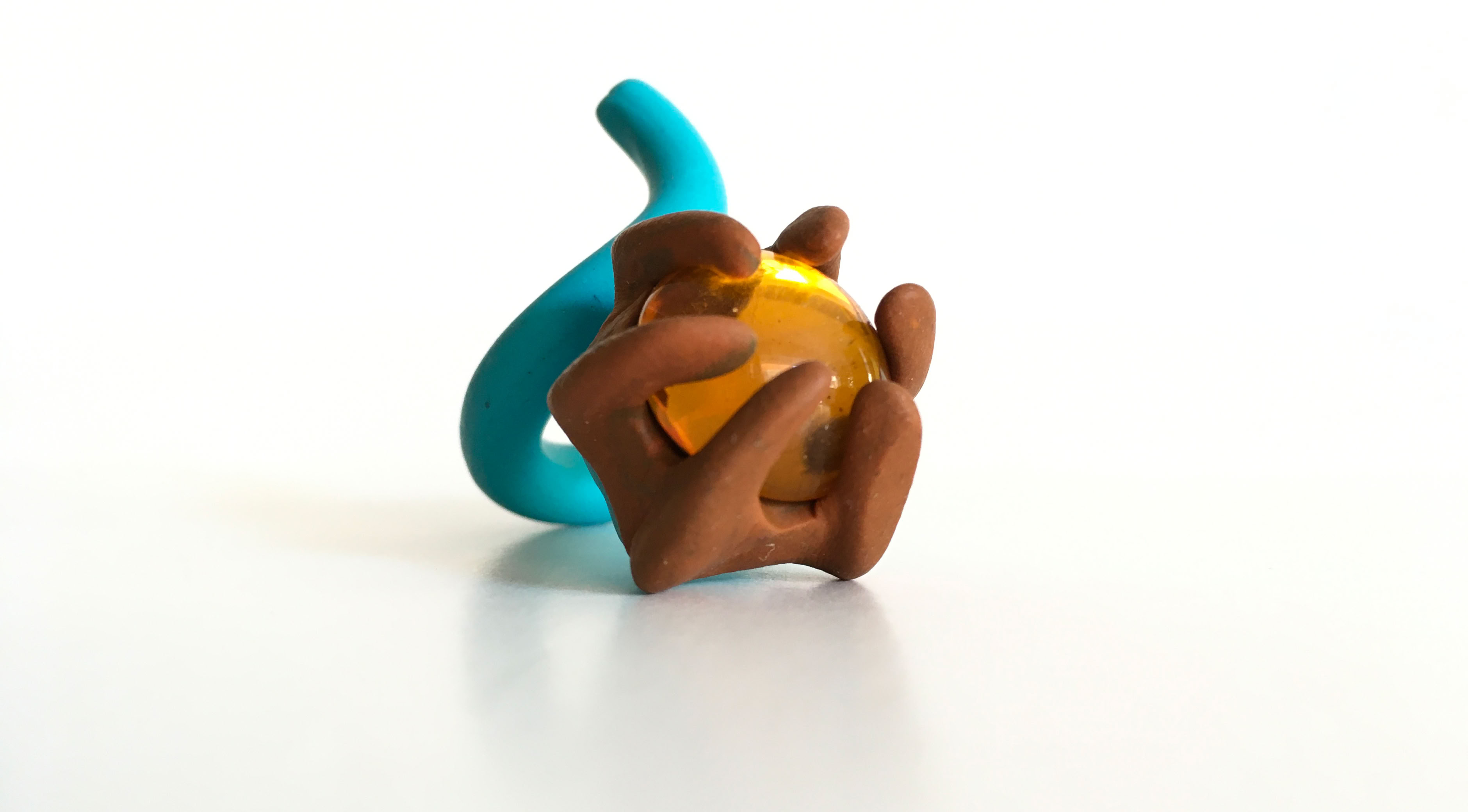 Sculpture abstraite en pâte à modeler avec des formes marron et bleues autour d'une sphère jaune.