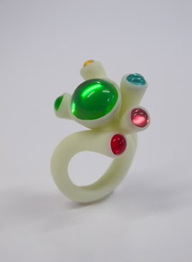 Bague blanche avec des pierres colorées vertes, rouges et bleues.