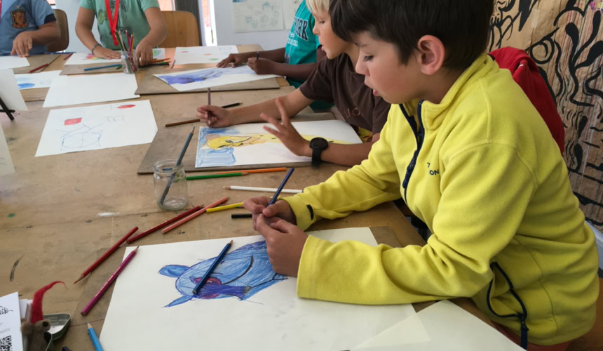 Des enfants assis à une table en train de dessiner avec des crayons de couleur.