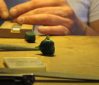 Mains travaillant sur une pièce de bois avec des outils et de la cire verte sur une table.