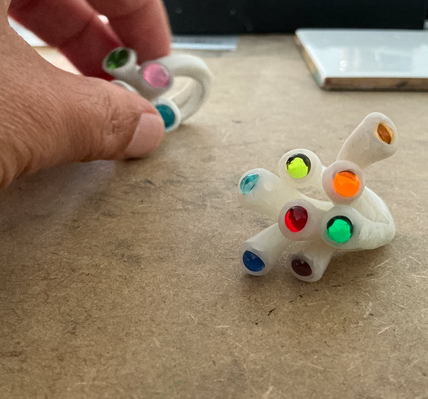 Travail à la main d'une bague en résine blanche avec des perles colorés, posé sur une surface en bois.