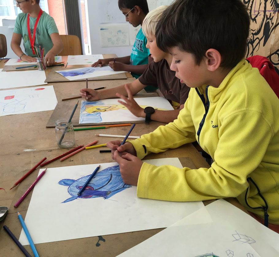 Des enfants assis à une table en train de dessiner avec des crayons de couleur.