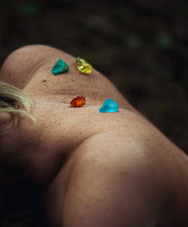 Corps allongé avec des pierres colorées sur le dos, dans un environnement naturel.