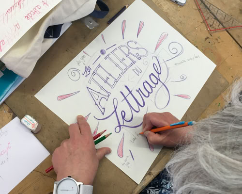 Personne faisant de la calligraphie sur une feuille de papier avec des crayons, avec les mots "ATELIERS de lettrage" visibles.