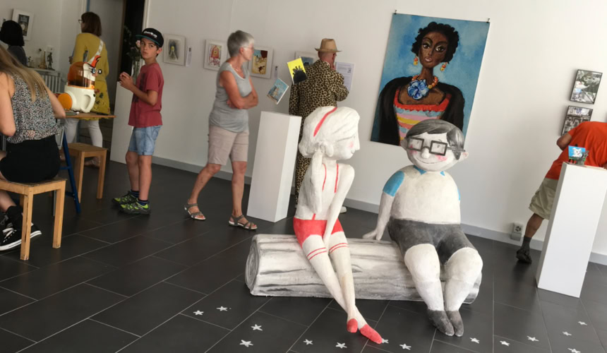 Galerie d'art avec sculptures sur socles blancs et plusieurs peintures accrochées au mur.