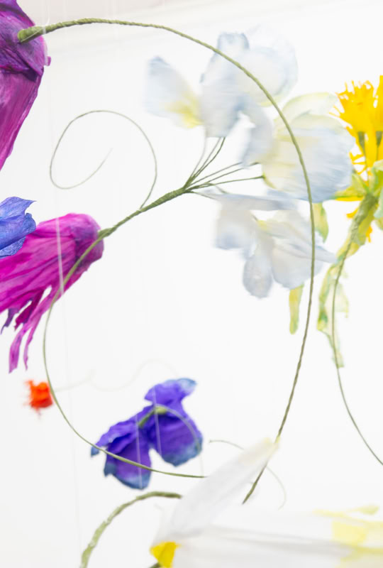 Fleurs colorées en papier suspendues dans les airs sur un fond blanc.
