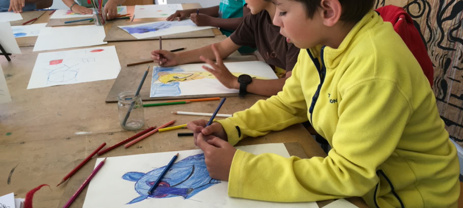 Des enfants assis à une table en train de dessiner avec des crayons de couleur.