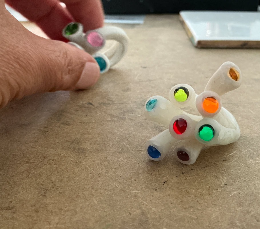 Travail à la main d'une bague en résine blanche avec des perles colorés, posé sur une surface en bois.