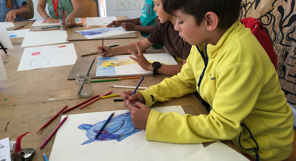 Des enfants assis à une table en train de dessiner avec des crayons de couleur.