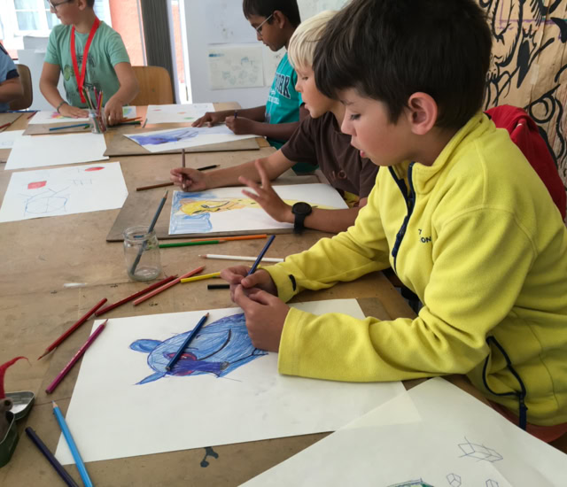 Des enfants assis à une table en train de dessiner avec des crayons de couleur.