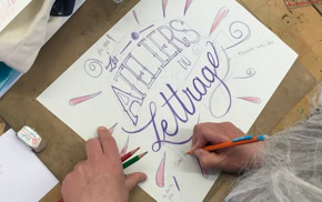 Personne faisant de la calligraphie sur une feuille de papier avec des crayons, avec les mots "ATELIERS de lettrage" visibles.