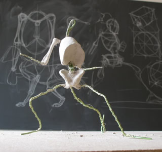 Petite sculpture en fil de fer et papier devant un tableau noir avec des dessins à la craie.