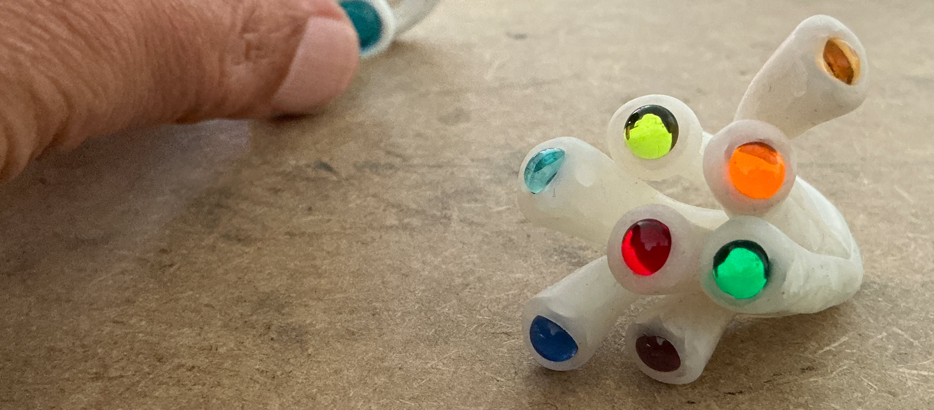 Travail à la main d'une bague en résine blanche avec des perles colorés, posé sur une surface en bois.