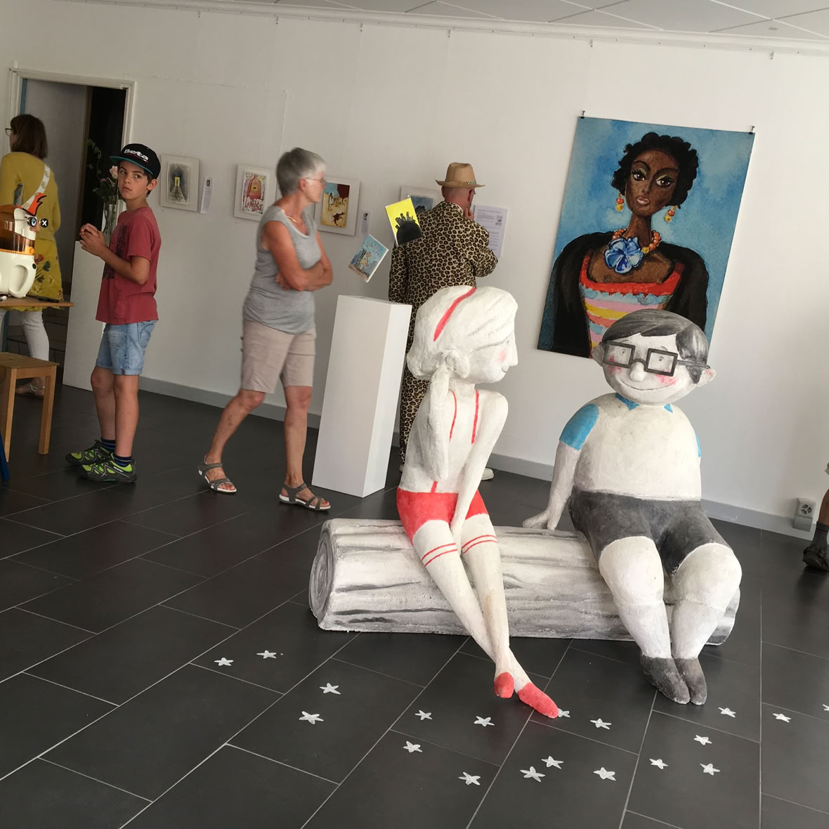 Galerie d'art avec sculptures sur socles blancs et plusieurs peintures accrochées au mur.