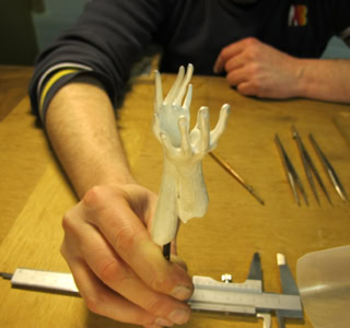 Personne tenant une sculpture blanche en forme de main sur une table avec des outils.
