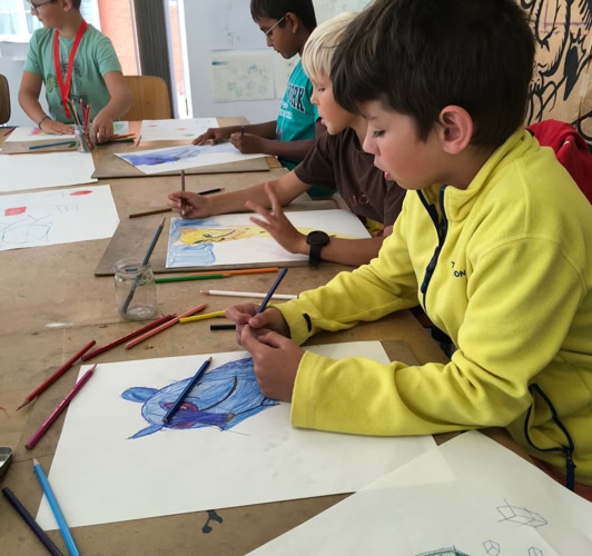 Des enfants assis à une table en train de dessiner avec des crayons de couleur.