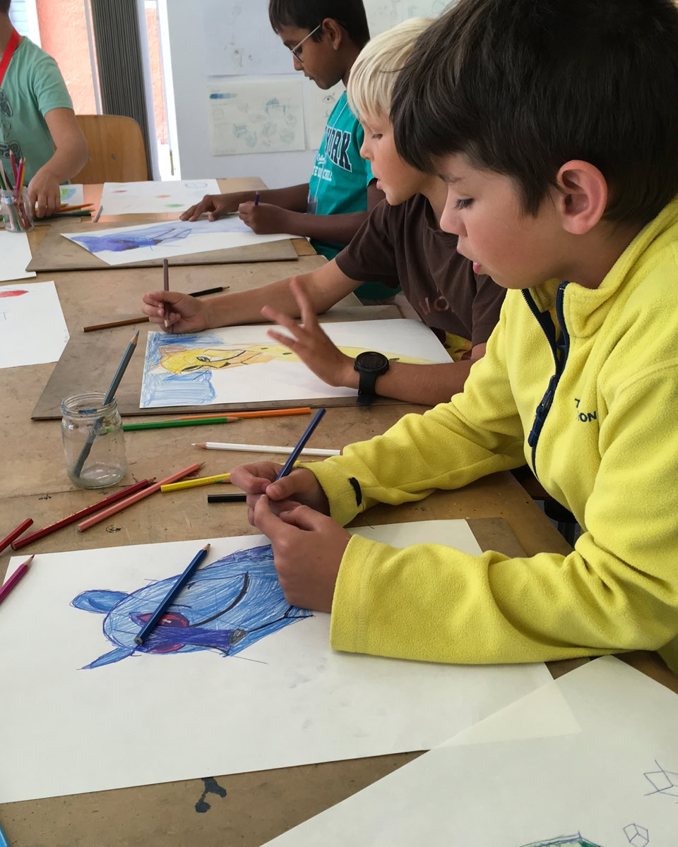 Des enfants assis à une table en train de dessiner avec des crayons de couleur.