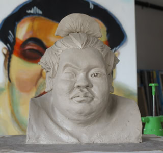 Buste en argile d'une personne avec un chignon, devant une peinture floue en arrière-plan.