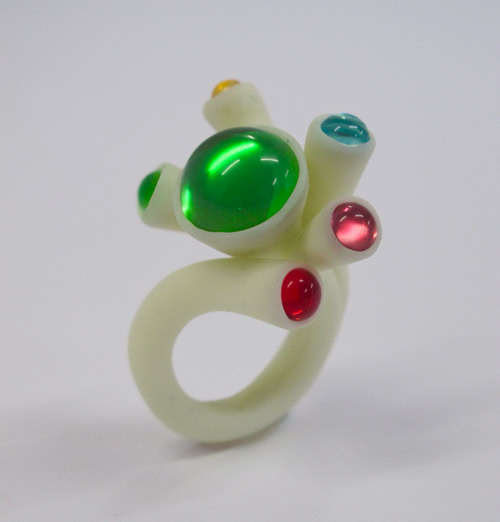 Bague blanche avec des pierres colorées vertes, rouges et bleues.