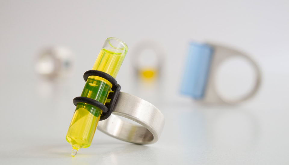 Création de bague en métal avec un tube à essai jaune, floue en arrière-plan d'autres bagues similaires.
