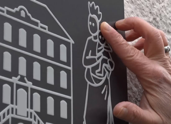 Main tenant une plaque avec des dessins en relief d'un bâtiment et d'une figure humaine.