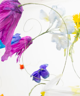 Fleurs colorées en papier suspendues dans les airs sur un fond blanc.