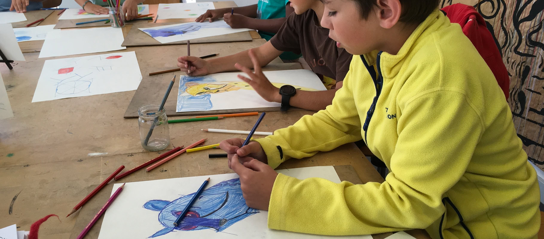 Des enfants assis à une table en train de dessiner avec des crayons de couleur.
