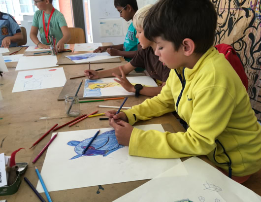 Des enfants assis à une table en train de dessiner avec des crayons de couleur.