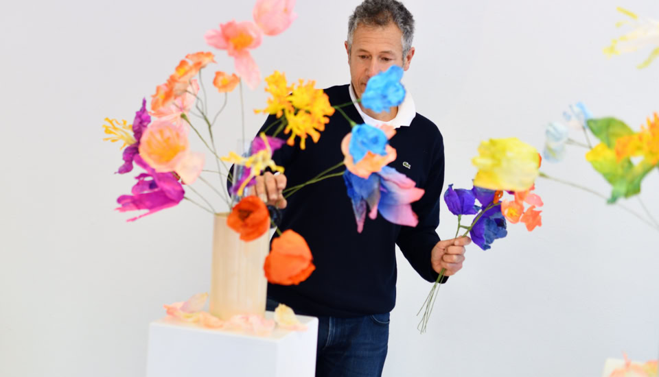 Deux personnes assises à une table en train de dessiner, avec des crayons de couleur, des carnets de croquis et d'autres fournitures artistiques dispersés sur la table.