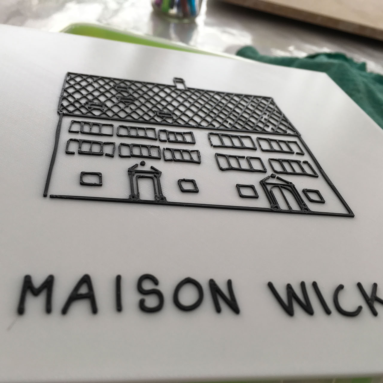 Plaque blanche avec un dessin d'une maison et le texte "MAISON WICKA" en dessous.