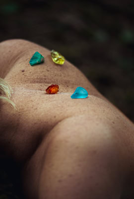 Corps allongé avec des pierres colorées sur le dos, dans un environnement naturel.