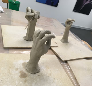 Sculptures en argile de mains sur des plaques en bois dans une salle d'art.