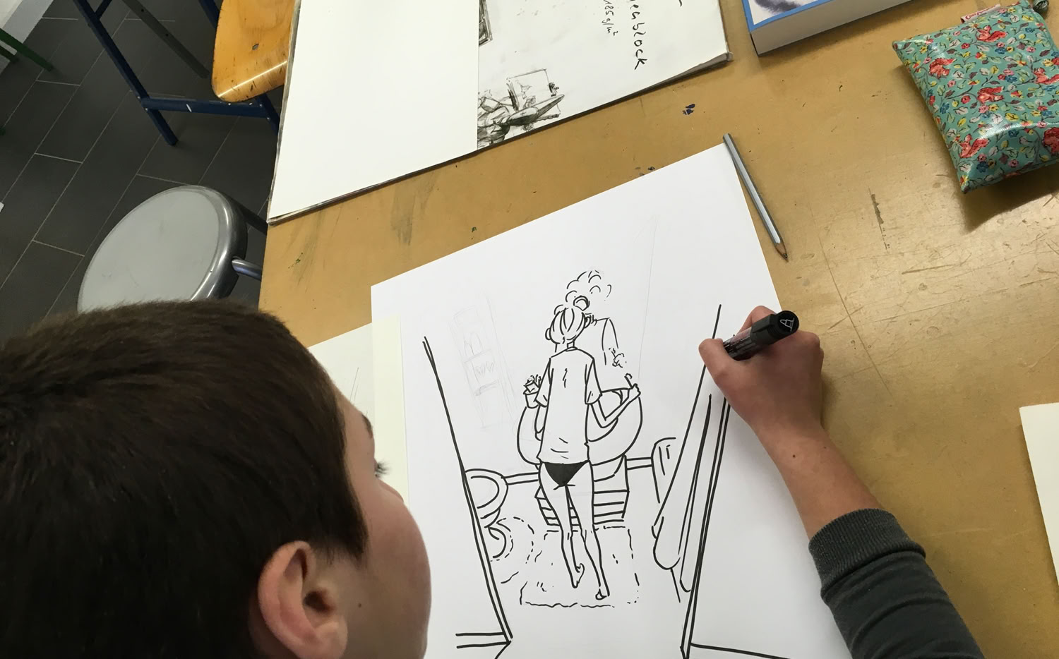 Un enfant dessine sur une feuille de papier, avec un dessin en noir et blanc représentant une personne marchant.