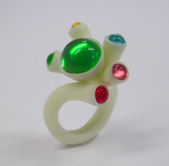Bague blanche avec des pierres colorées vertes, rouges et bleues.